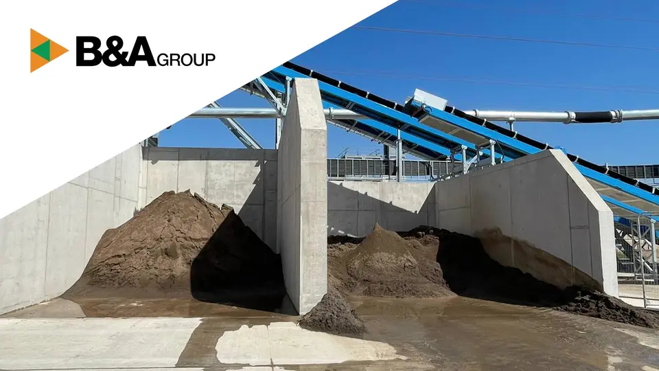B&A Group logo in the top left corner above an outdoor wash plant site with large piles of washed soil and aggregate stored in concrete bays, surrounded by conveyor belts under a clear blue sky.